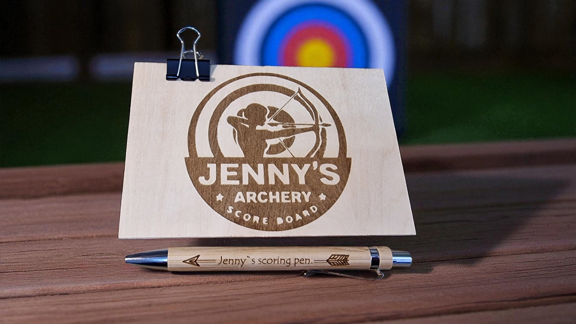 Jenny's Archery Score Board with pen on a wooden surface, archery target in the background