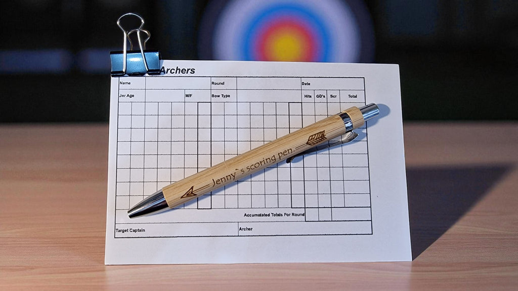 Wooden pen with branding on a target scoring sheet, blurred archery target in the background.