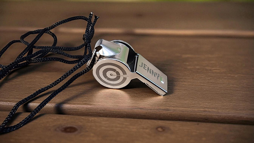 Silver whistle with black lanyard on a wooden surface
