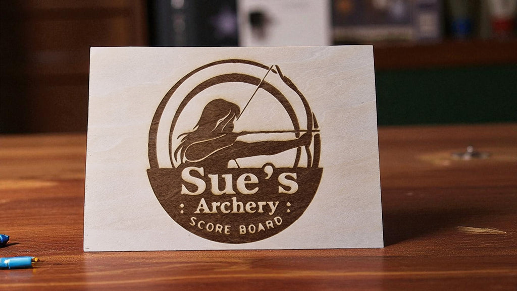 Scoreboard for Sue's Archery on a wooden surface with archery equipment in the background.