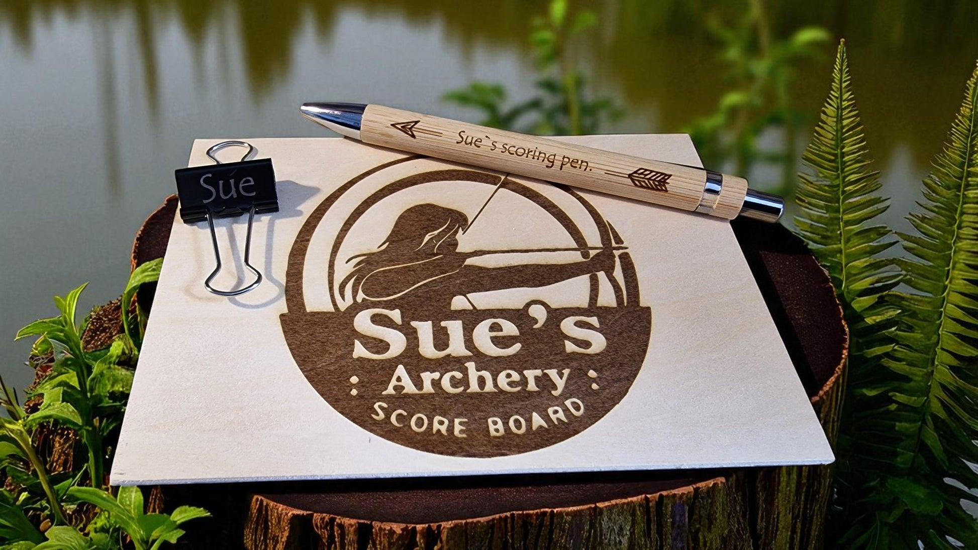 Scoreboard with 'Sue's Archery' branding and a pen on a natural background