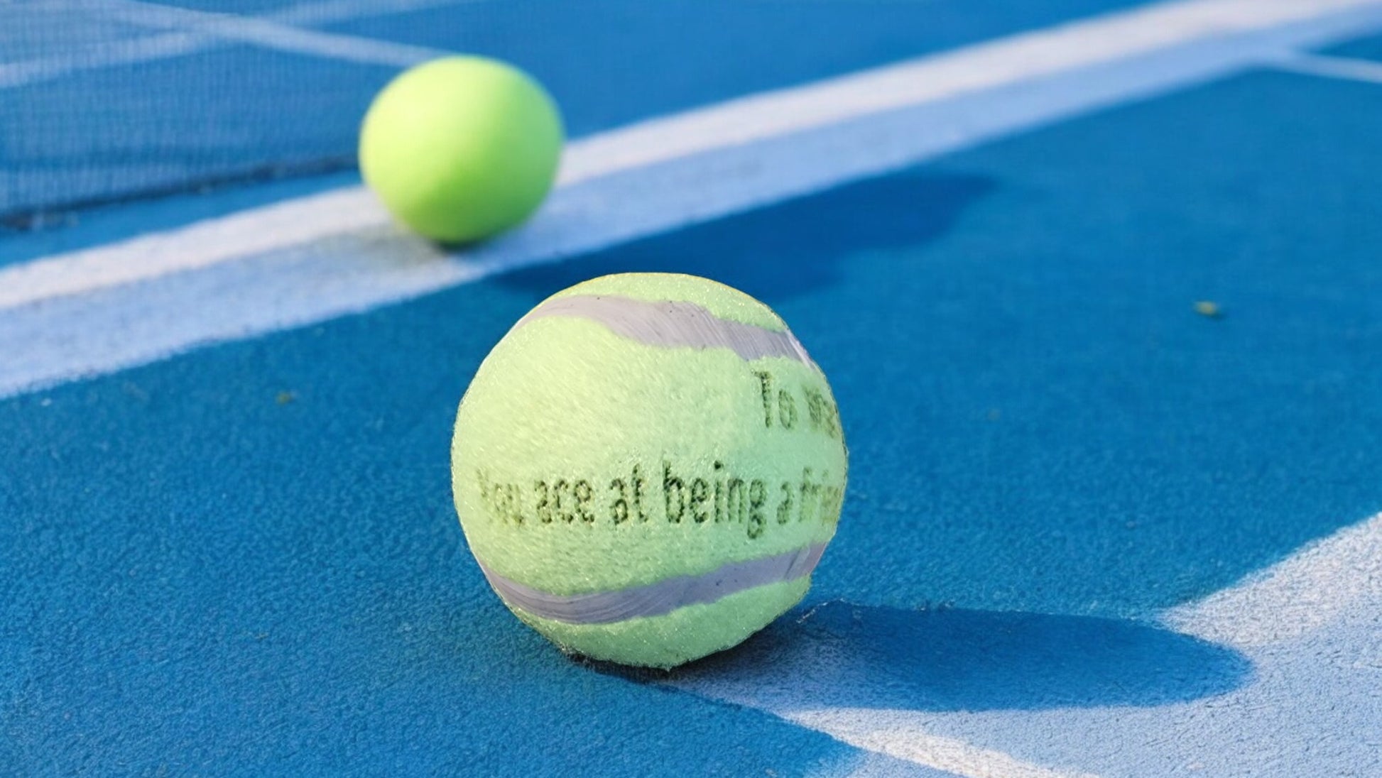 Tennis ball with text on a blue tennis court