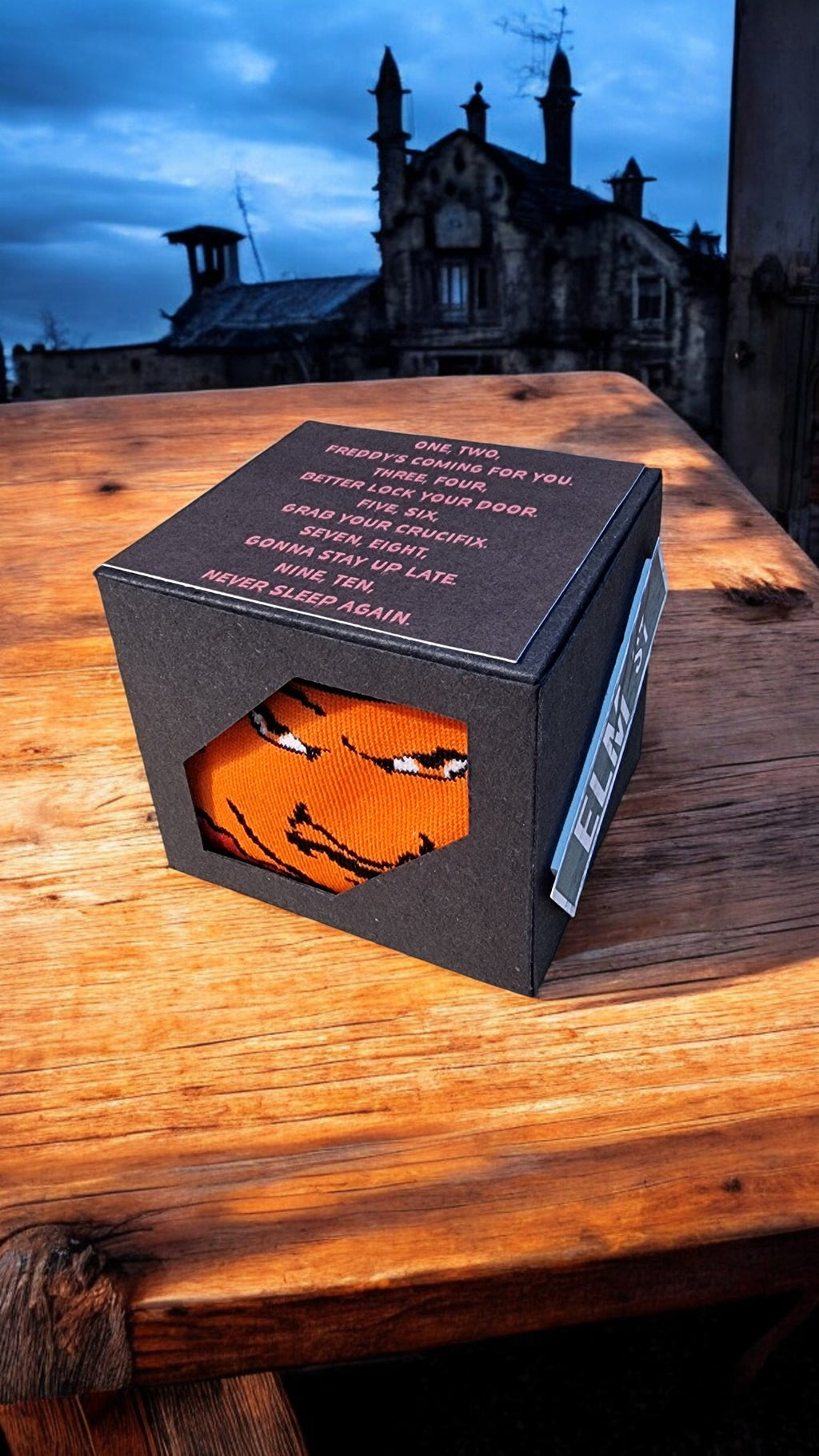Black box with an orange mask on a wooden surface at night.