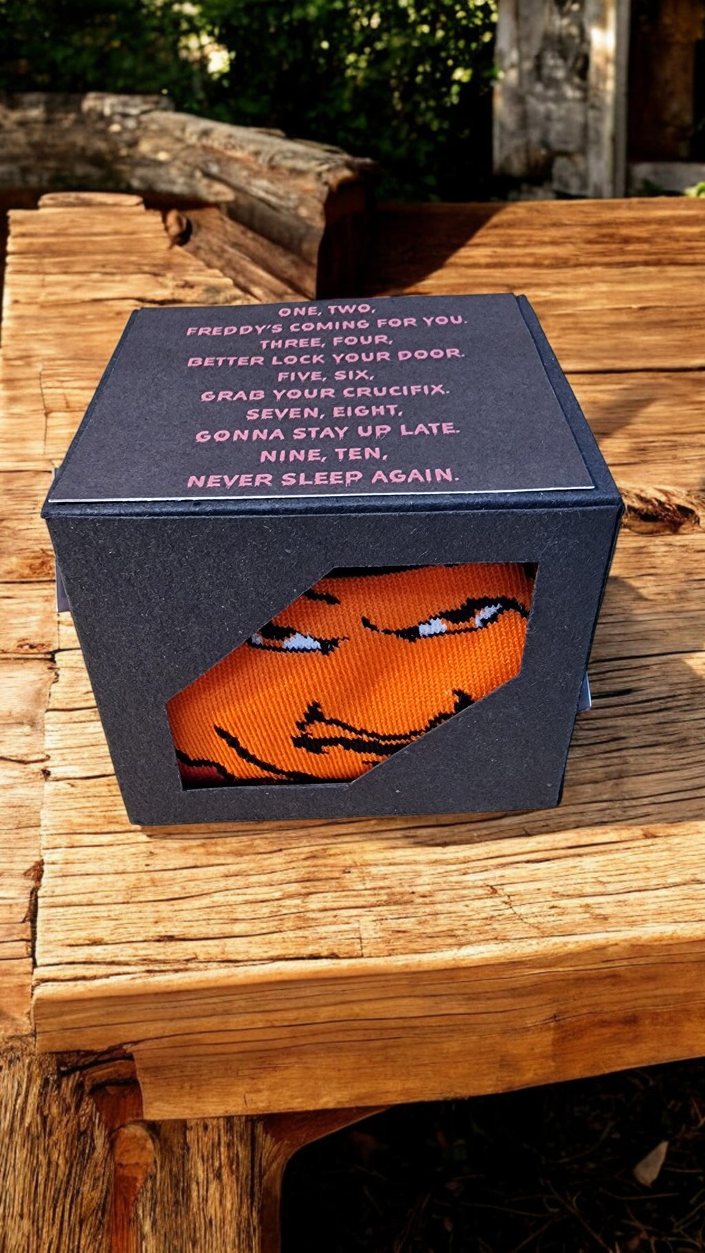 Orange sock with a face design in a black box on a wooden surface