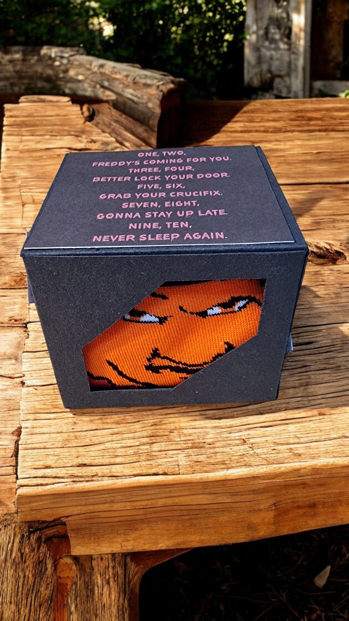 Orange sock with a face design in a black box on a wooden surface