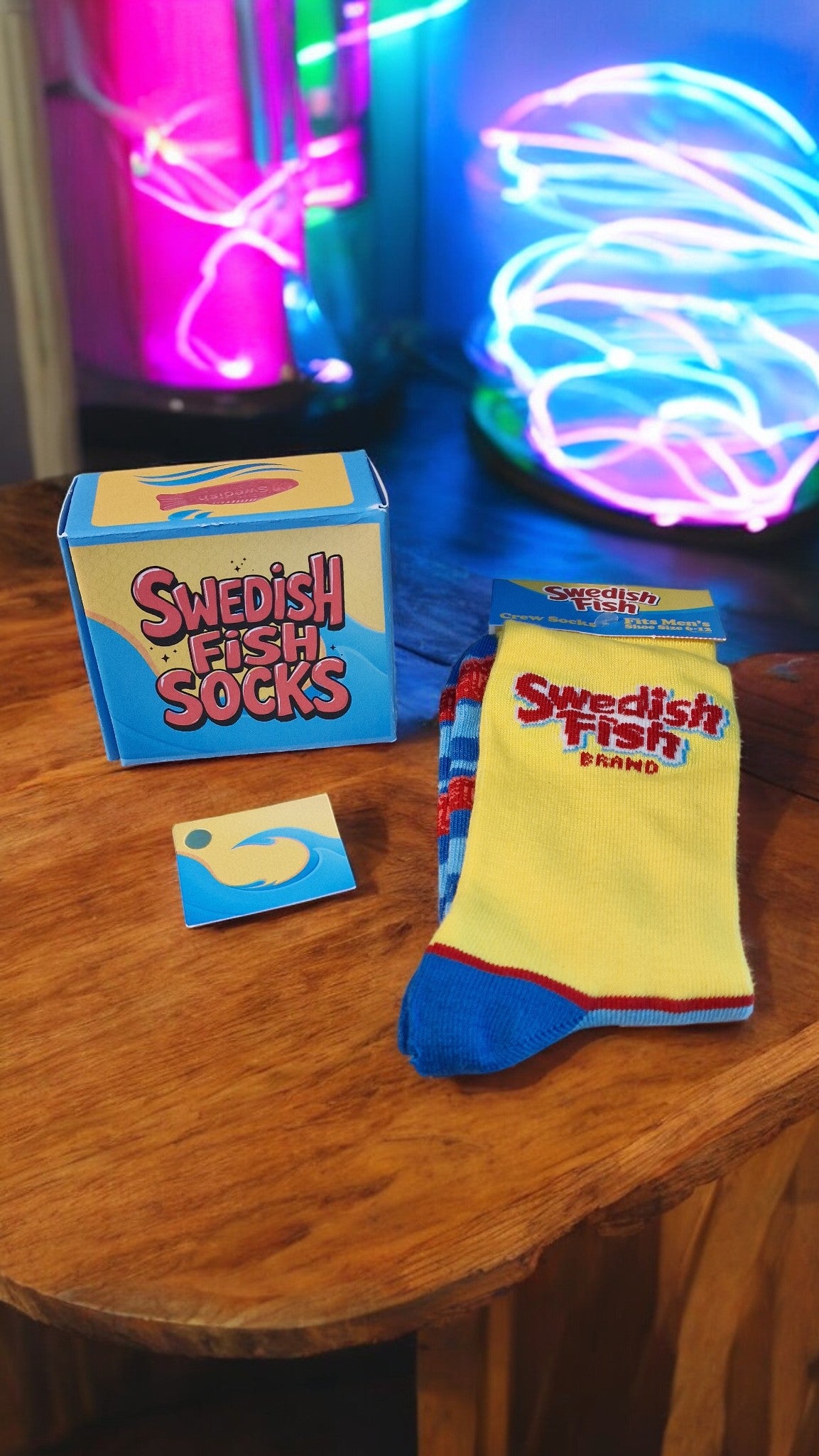 Swedish Fish socks and packaging on a wooden surface with neon lights in the background