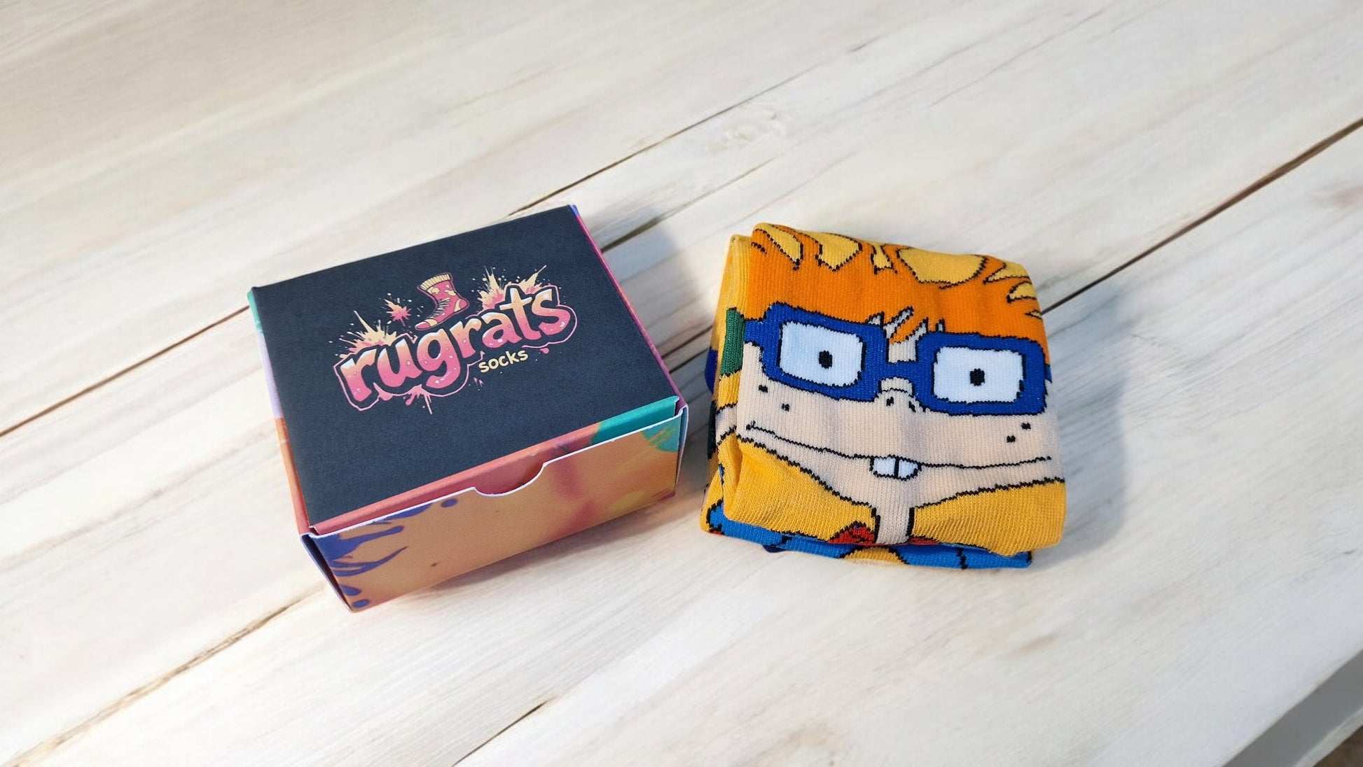 Box of 'rugrats' socks with a character-themed sock on a wooden surface