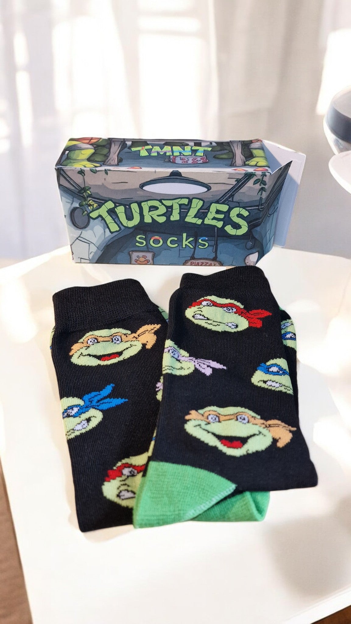 Two pairs of Teenage Mutant Ninja Turtles socks in front of their packaging box.