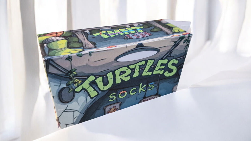 Box of turtle-themed socks on a white surface with light-colored curtains in the background