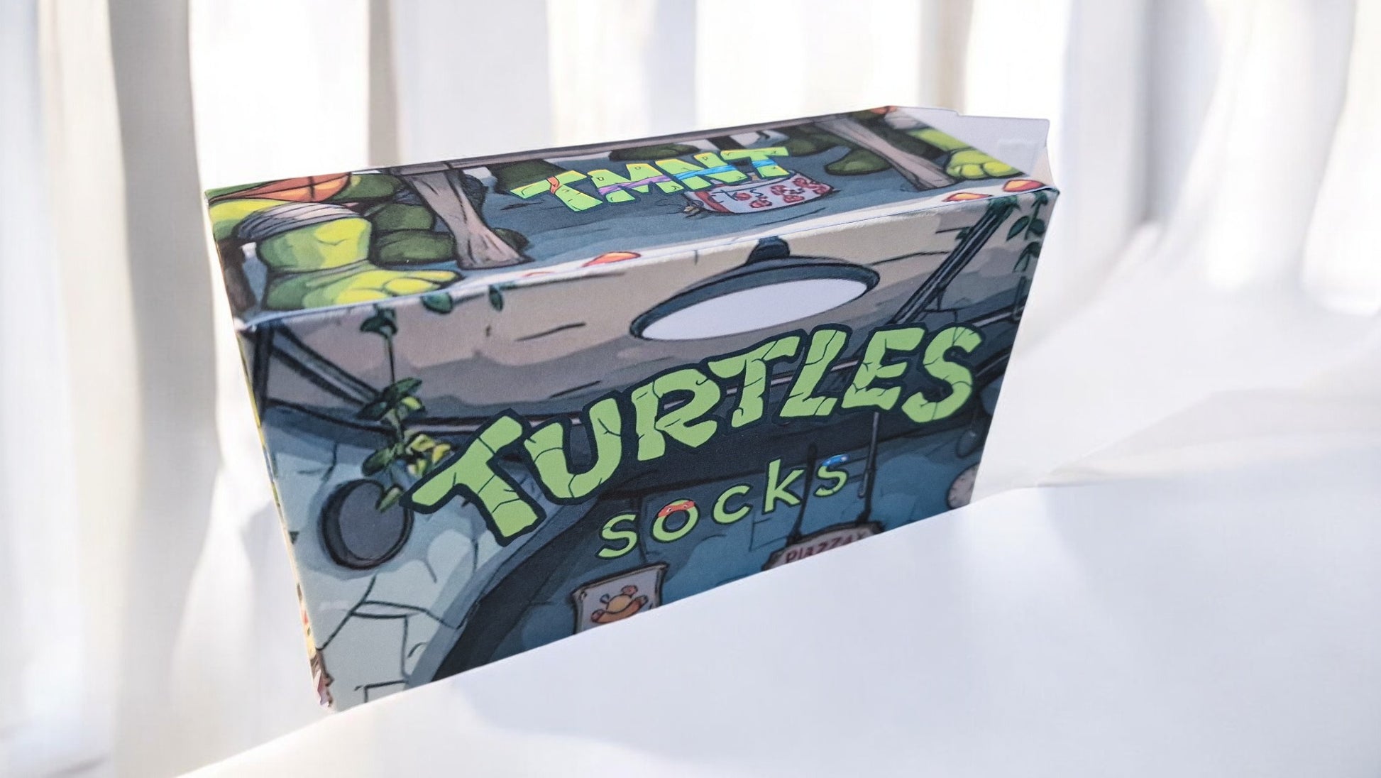 Box of turtle-themed socks on a white surface with light-colored curtains in the background