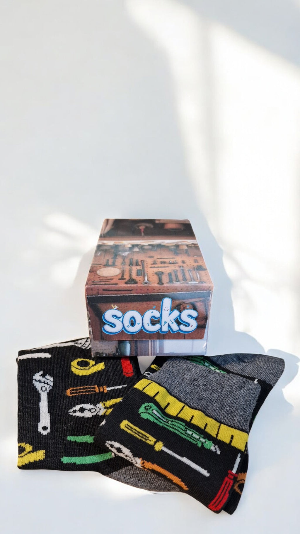 Pair of socks with tool design and a box labeled 'socks' on a white surface.