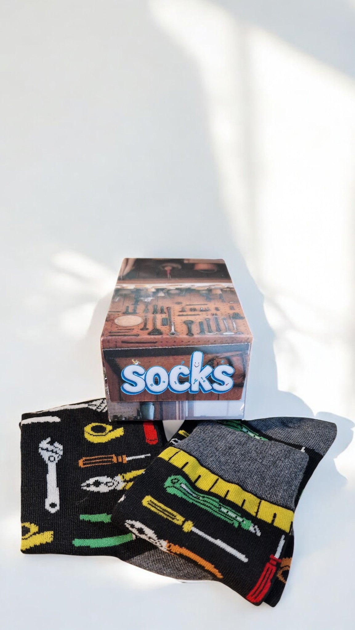 Pair of socks with tool design and a box labeled 'socks' on a white surface.
