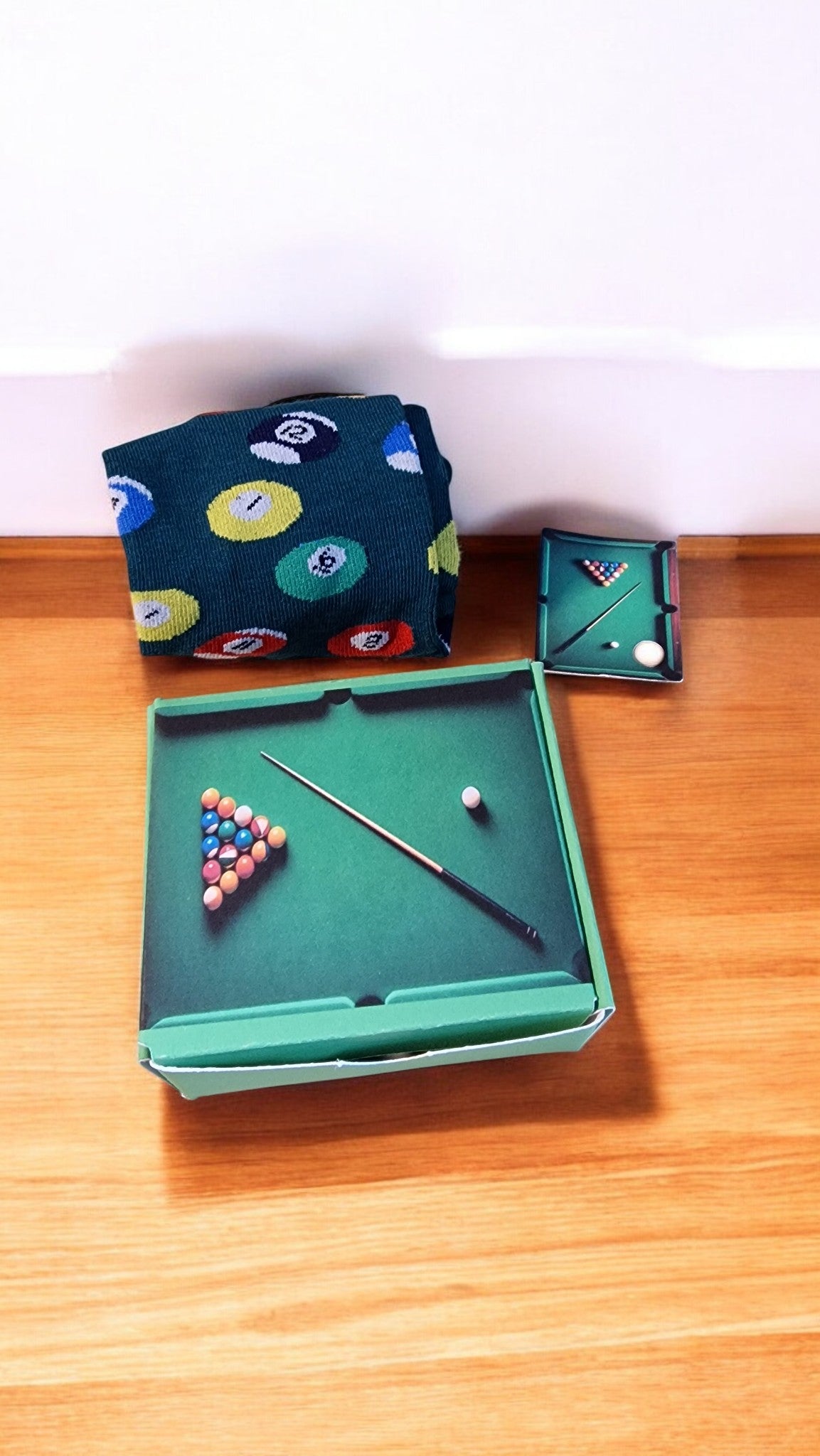 Miniature pool table set with balls and cue on a wooden surface