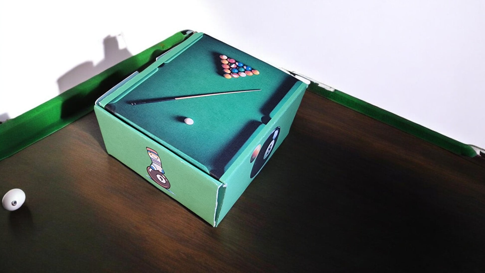 Pool table with a green felt pocket and pool balls on a wooden surface.