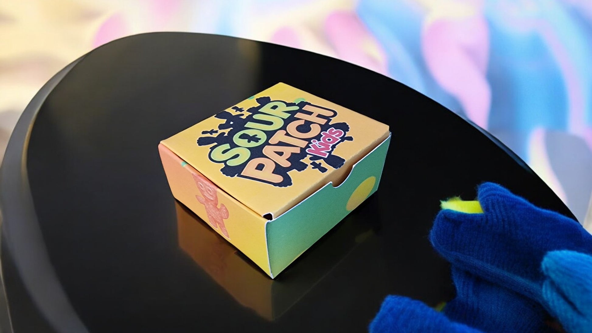 Sour Patch Kids box on a black surface with a colorful blurred background