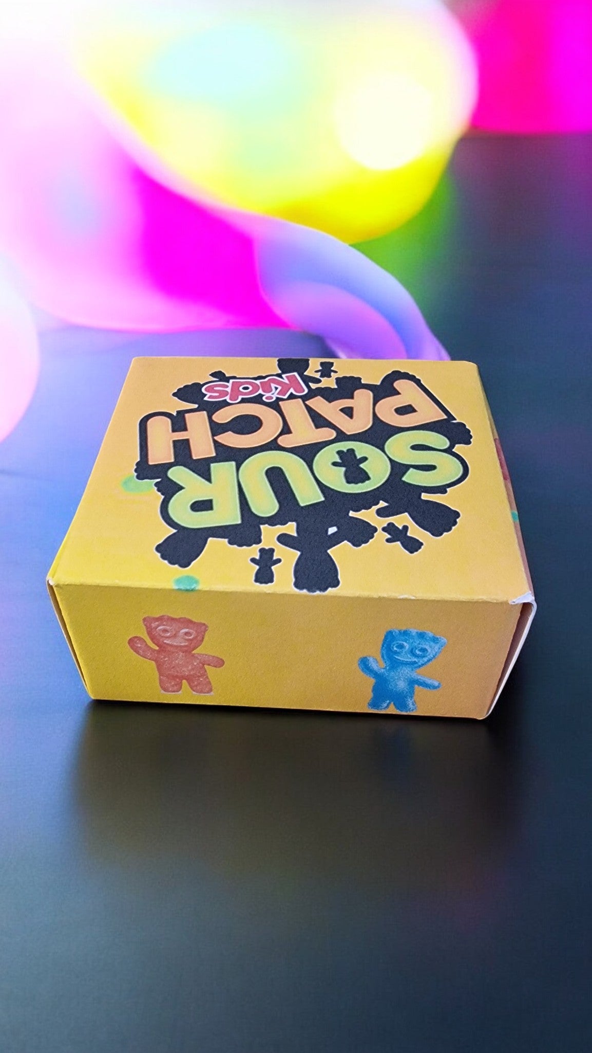 Yellow box with 'Sour Patch' branding on a dark surface with colorful light effects.