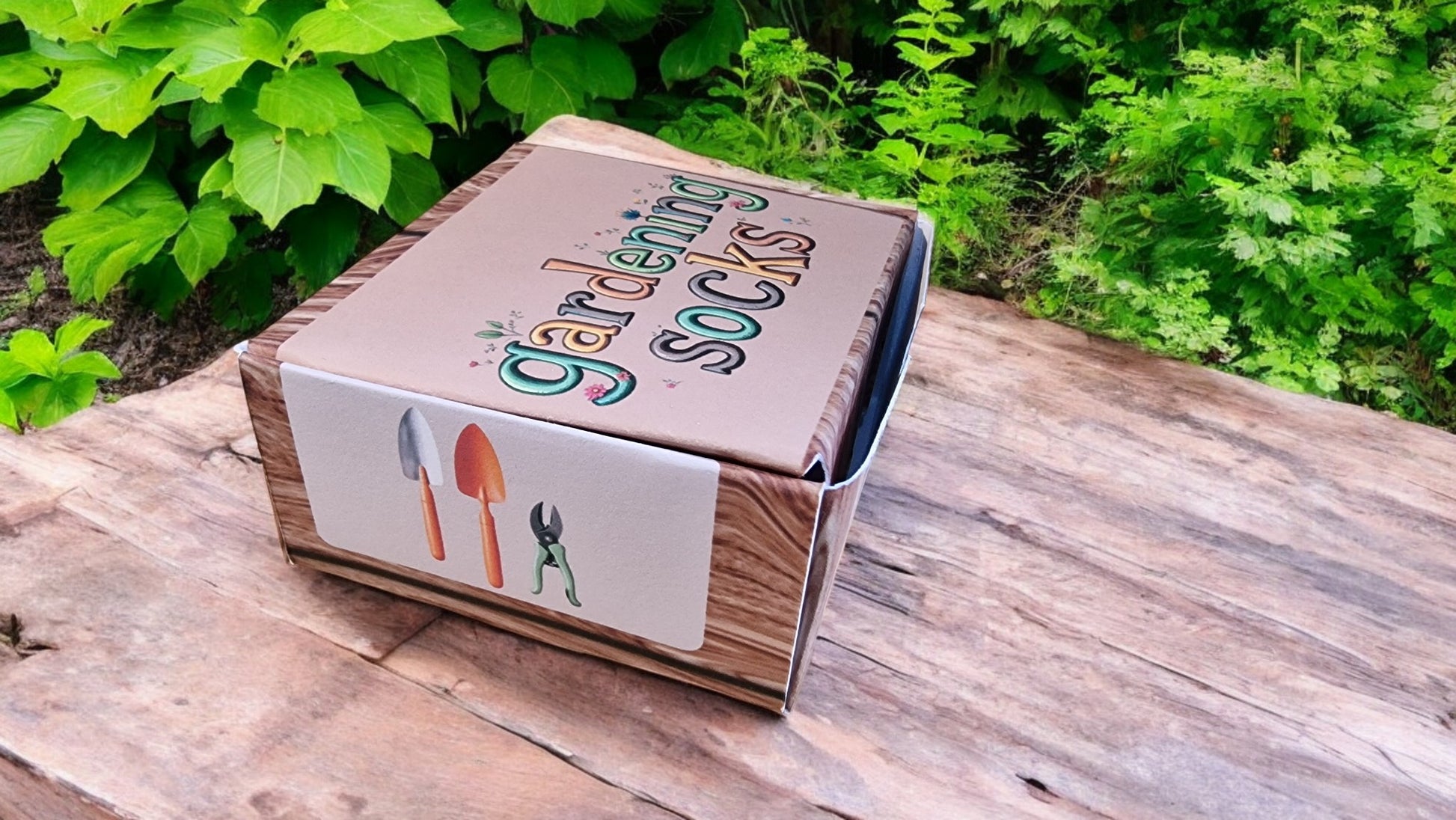 Box labeled 'Gardening Socks' on a wooden surface with greenery in the background