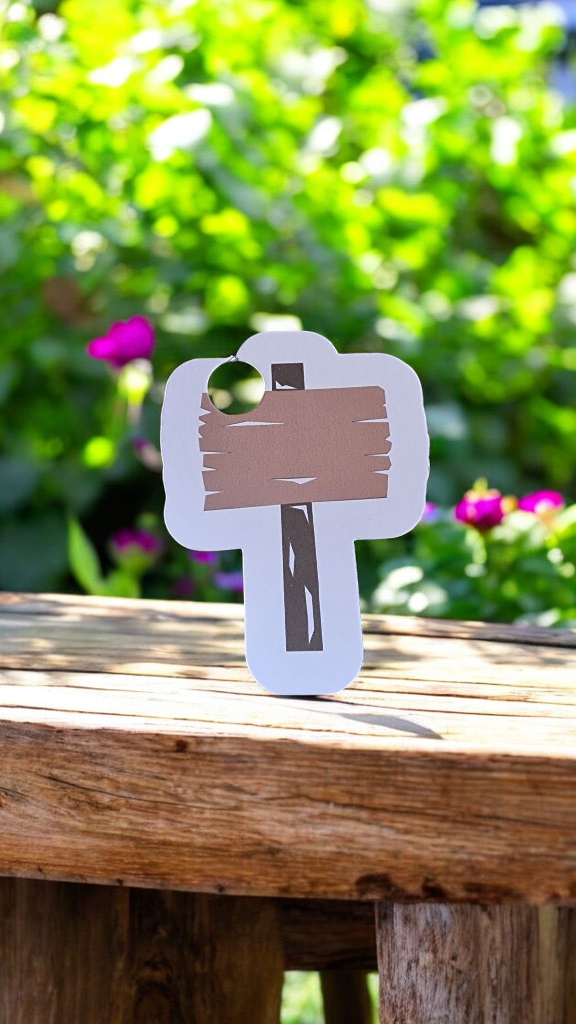Wooden signpost cutout on a wooden surface with a blurred green and pink floral background