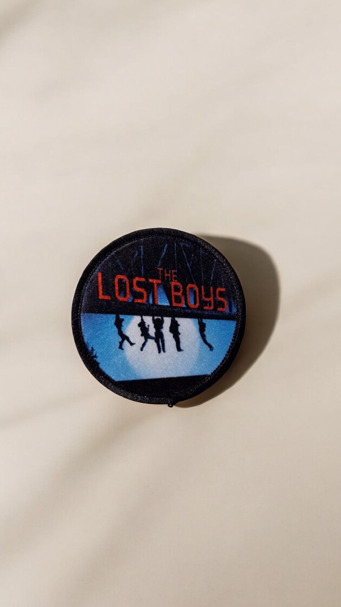 Round patch with 'The Lost Boys' text and silhouette design on a beige background
