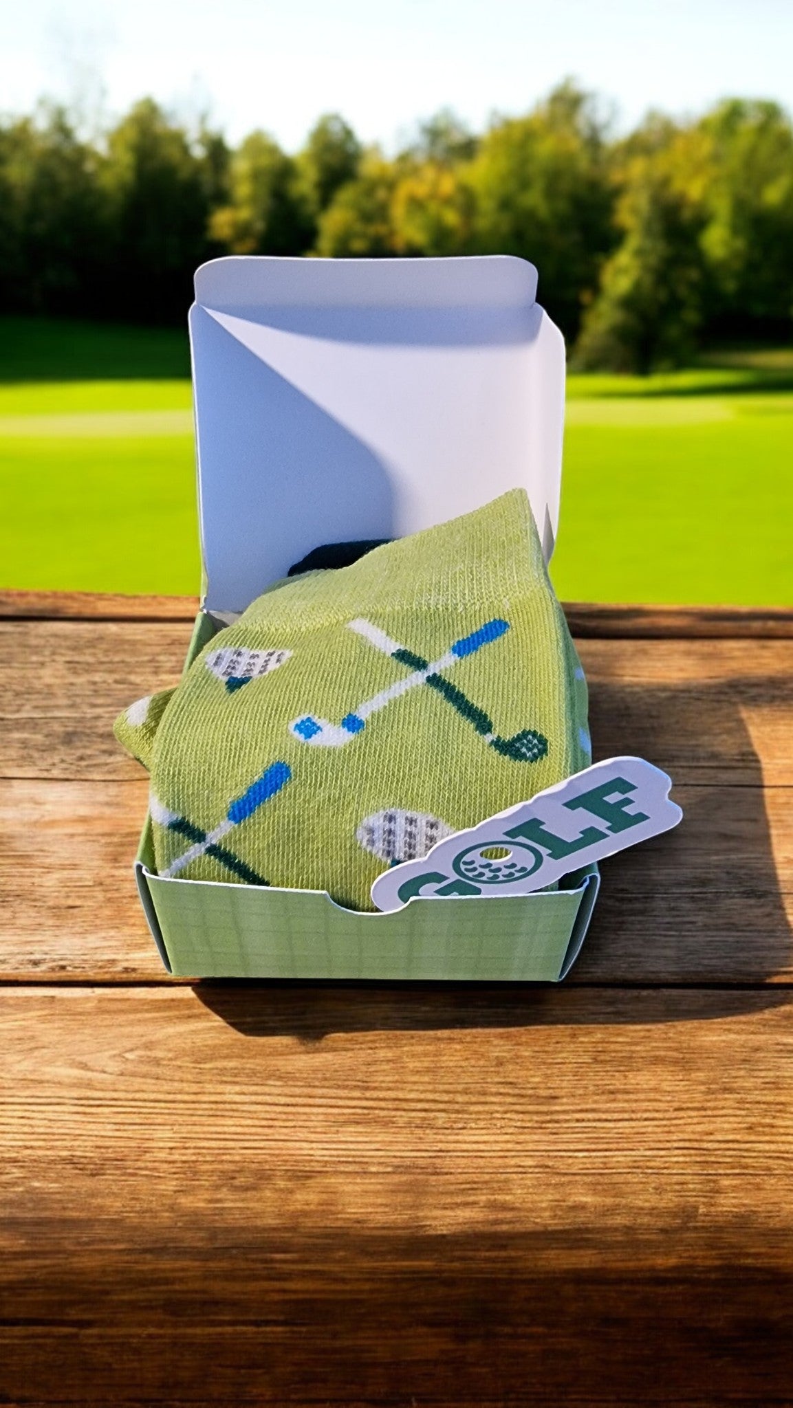 Green golf-themed socks in a box with a golf club design on a wooden surface.