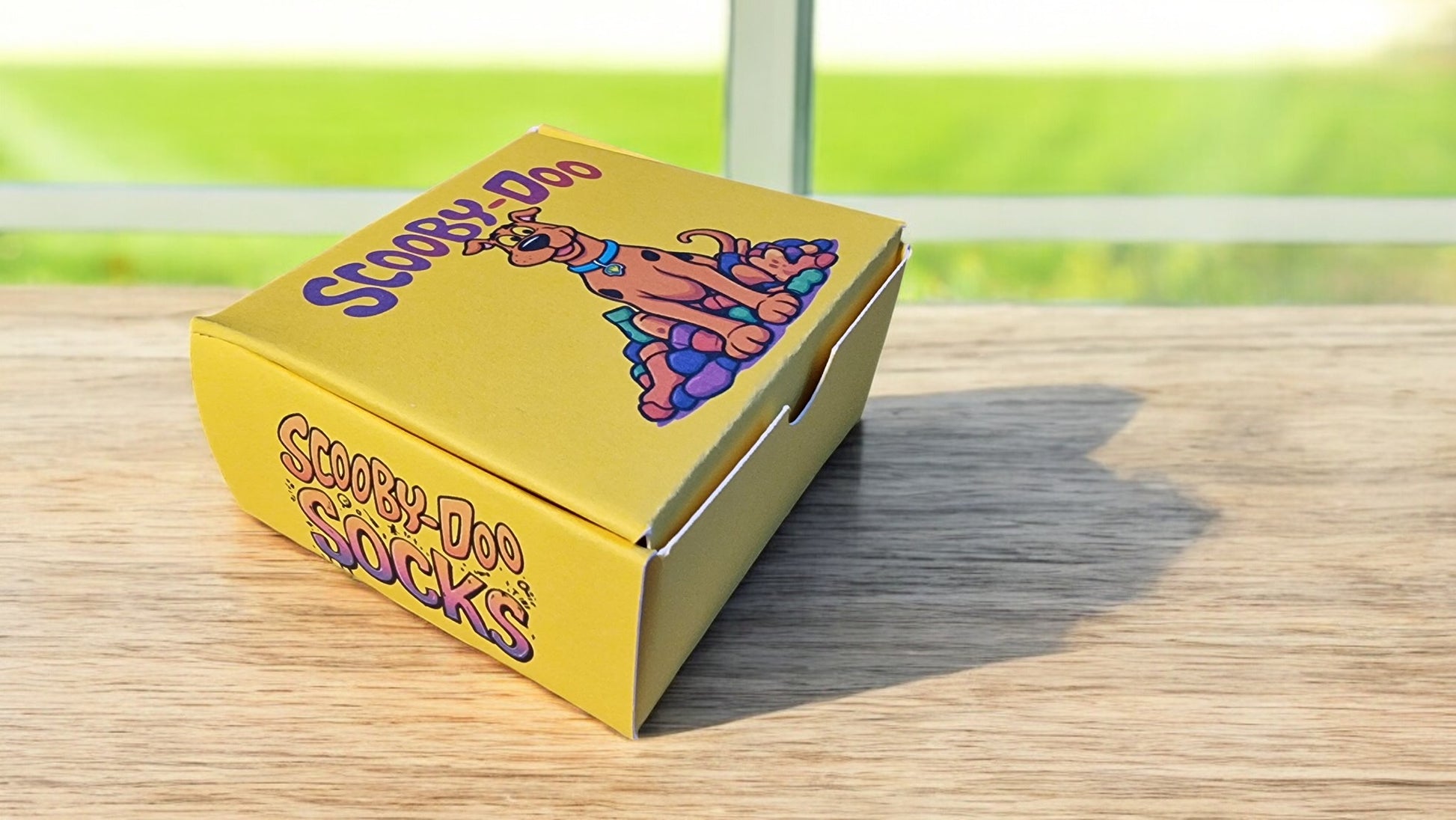 Yellow pizza box with 'Scooby-Doo' branding on a wooden surface.