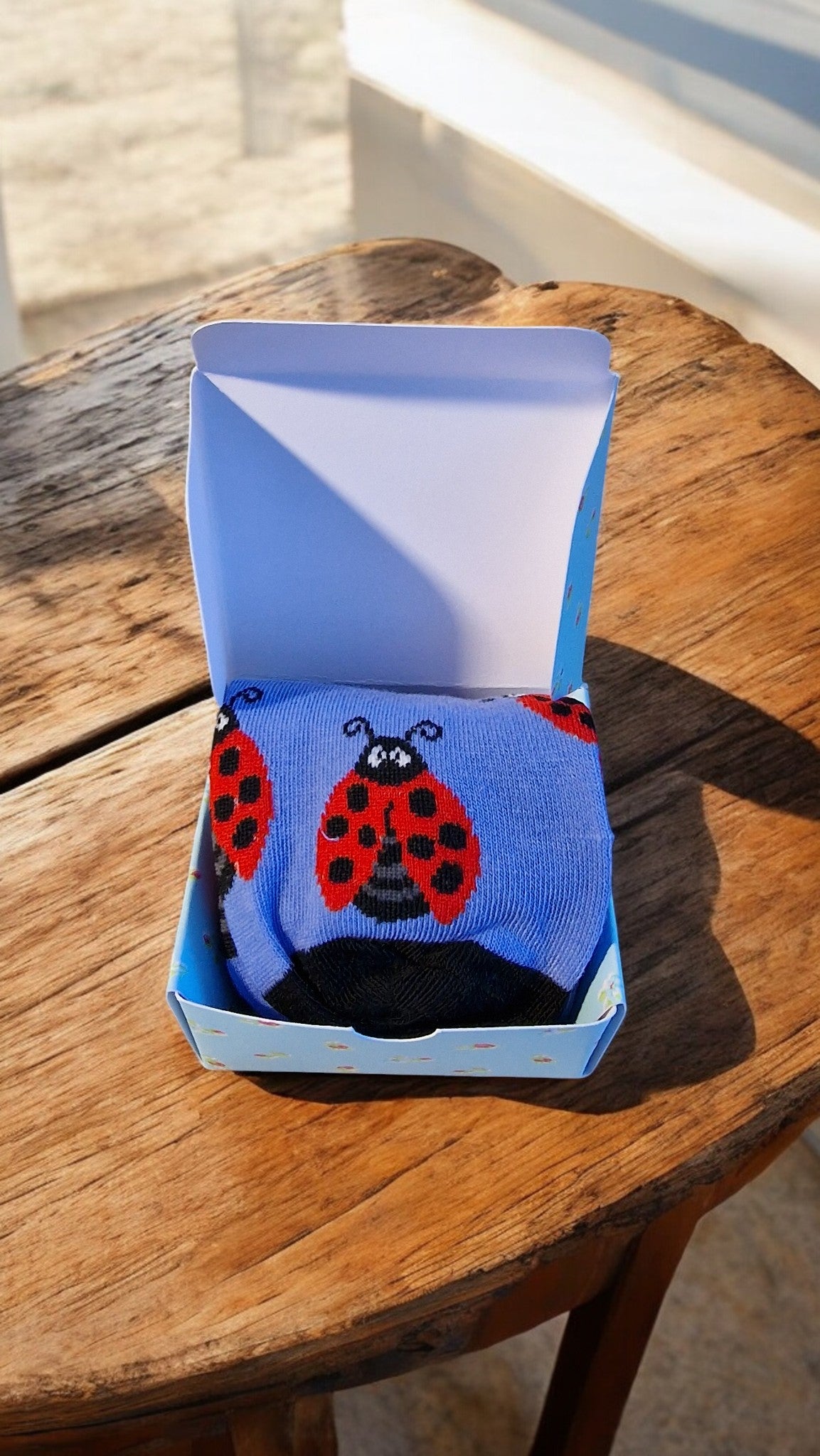 Blue sock with ladybug design in a box on a wooden surface