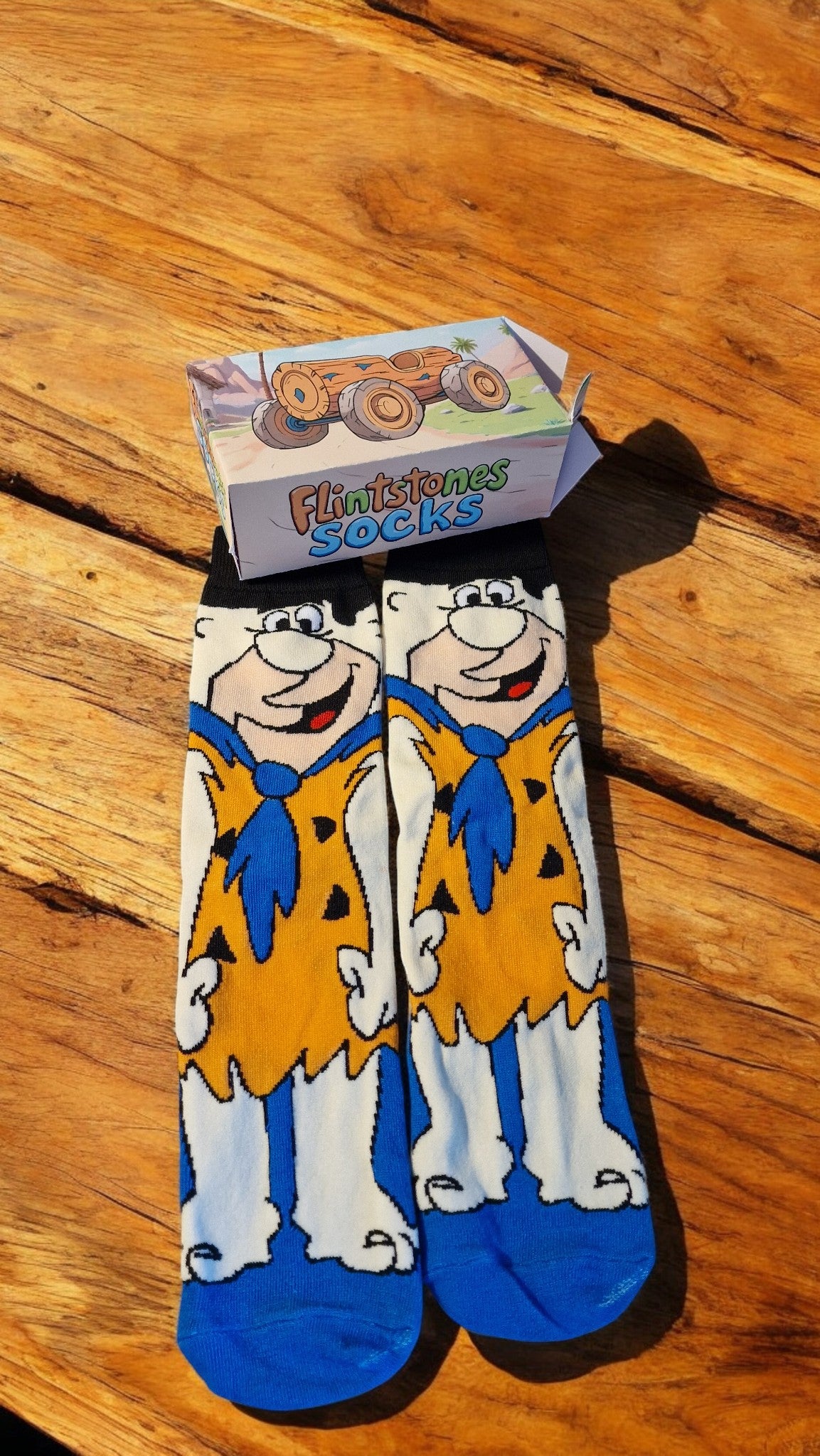 Cartoon character socks with a box labeled 'Flintstones Socks' on a wooden surface