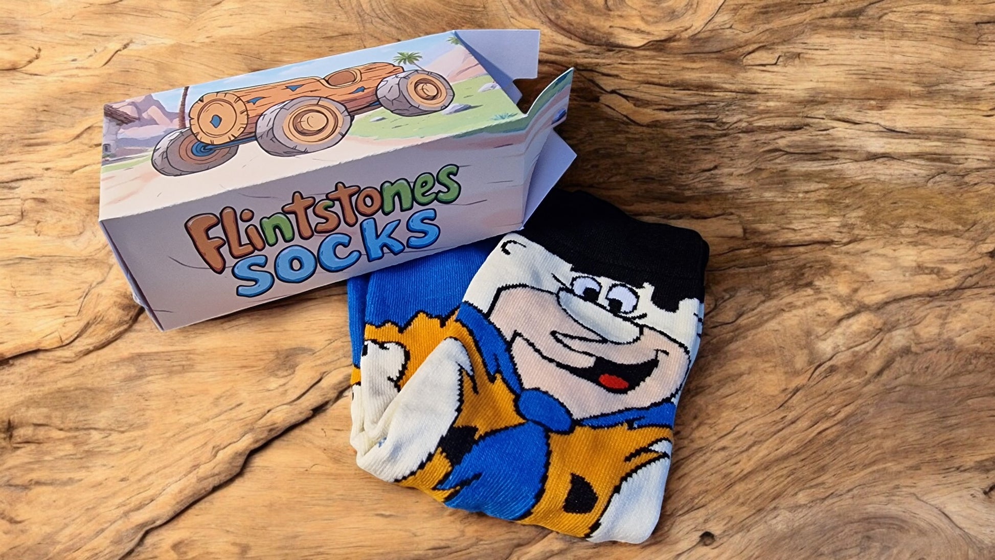 Pair of cartoon-themed socks with a box labeled 'Flintstones Socks' on a wooden surface