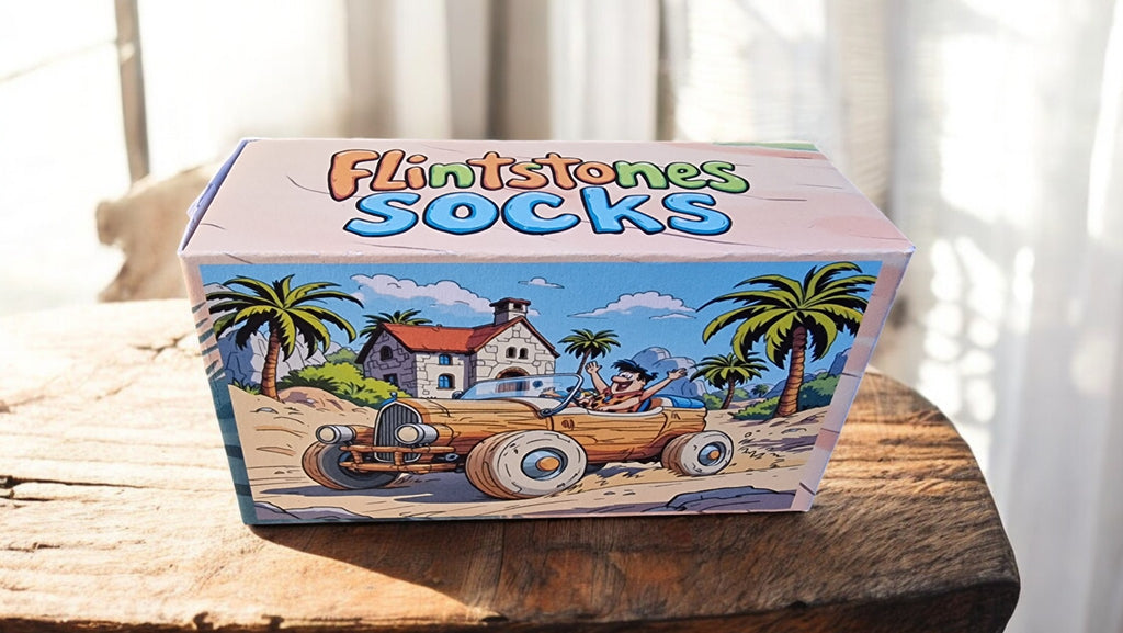 Box of Flintstones socks on a wooden surface with a beach scene illustration.