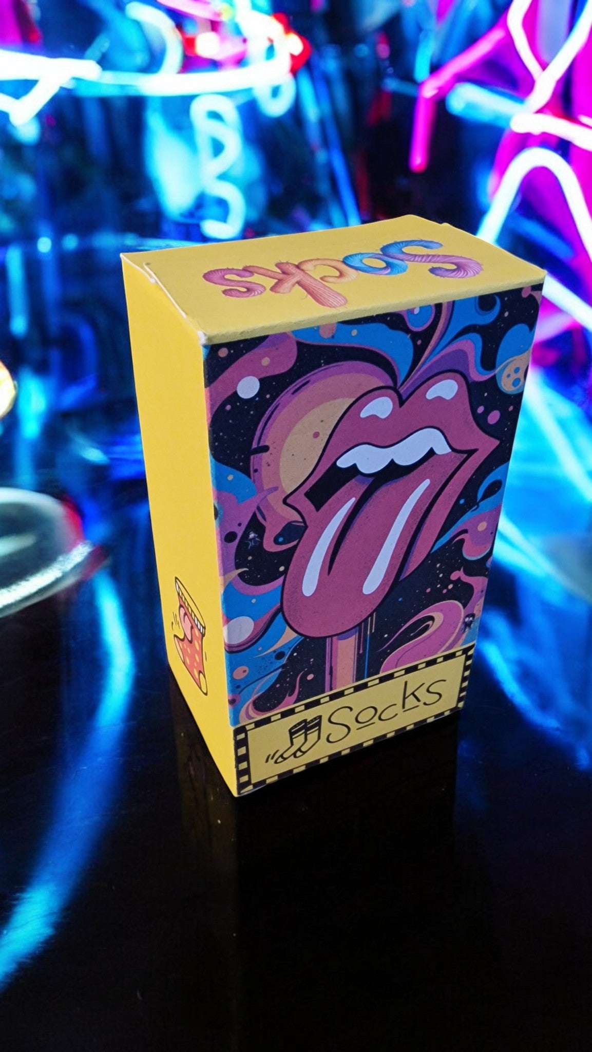 Box of socks with colorful design featuring a tongue and text, against a dark background with neon lights.