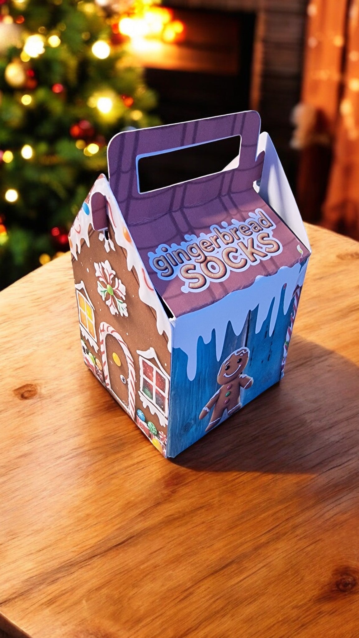 Gingerbread-themed gift box on a wooden surface with a blurred Christmas tree in the background.