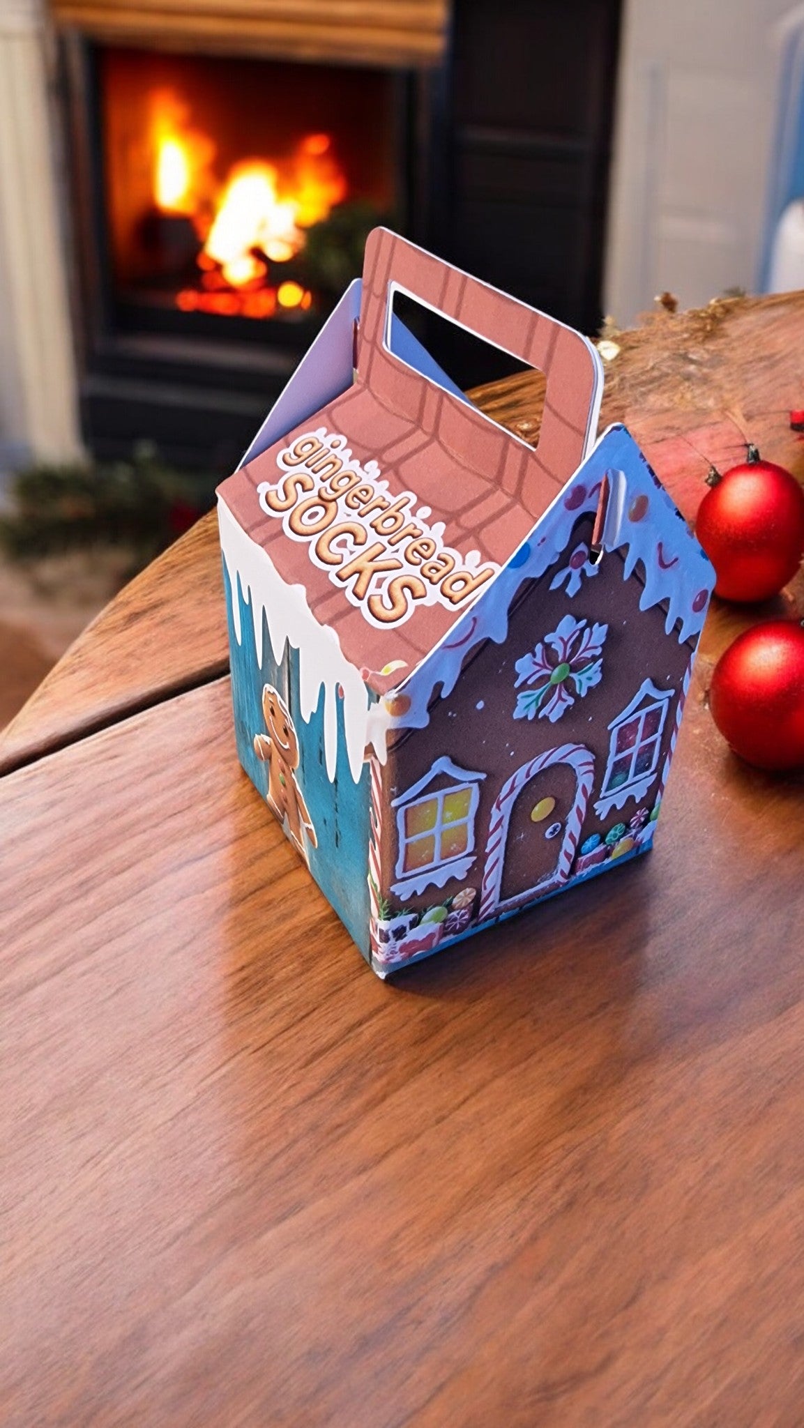 Gingerbread house-shaped box on a wooden surface with a fireplace in the background