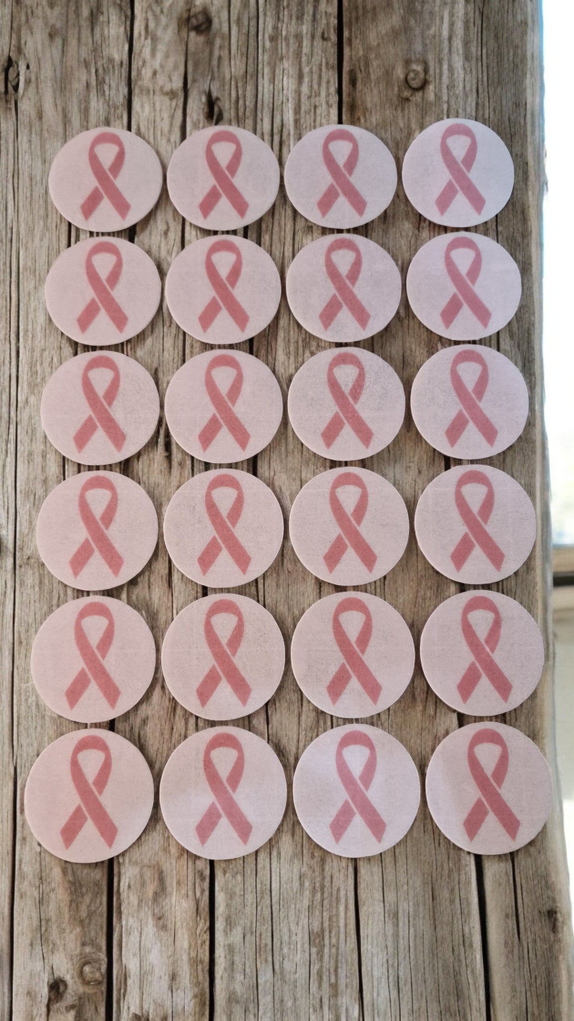 Multiple pink ribbons on round stickers against a wooden background
