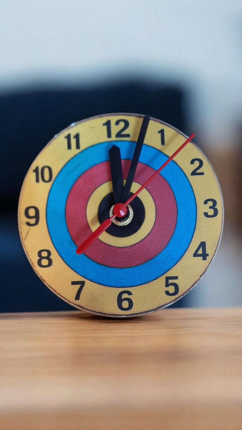 Colorful target-like clock on a wooden surface with a blurred background