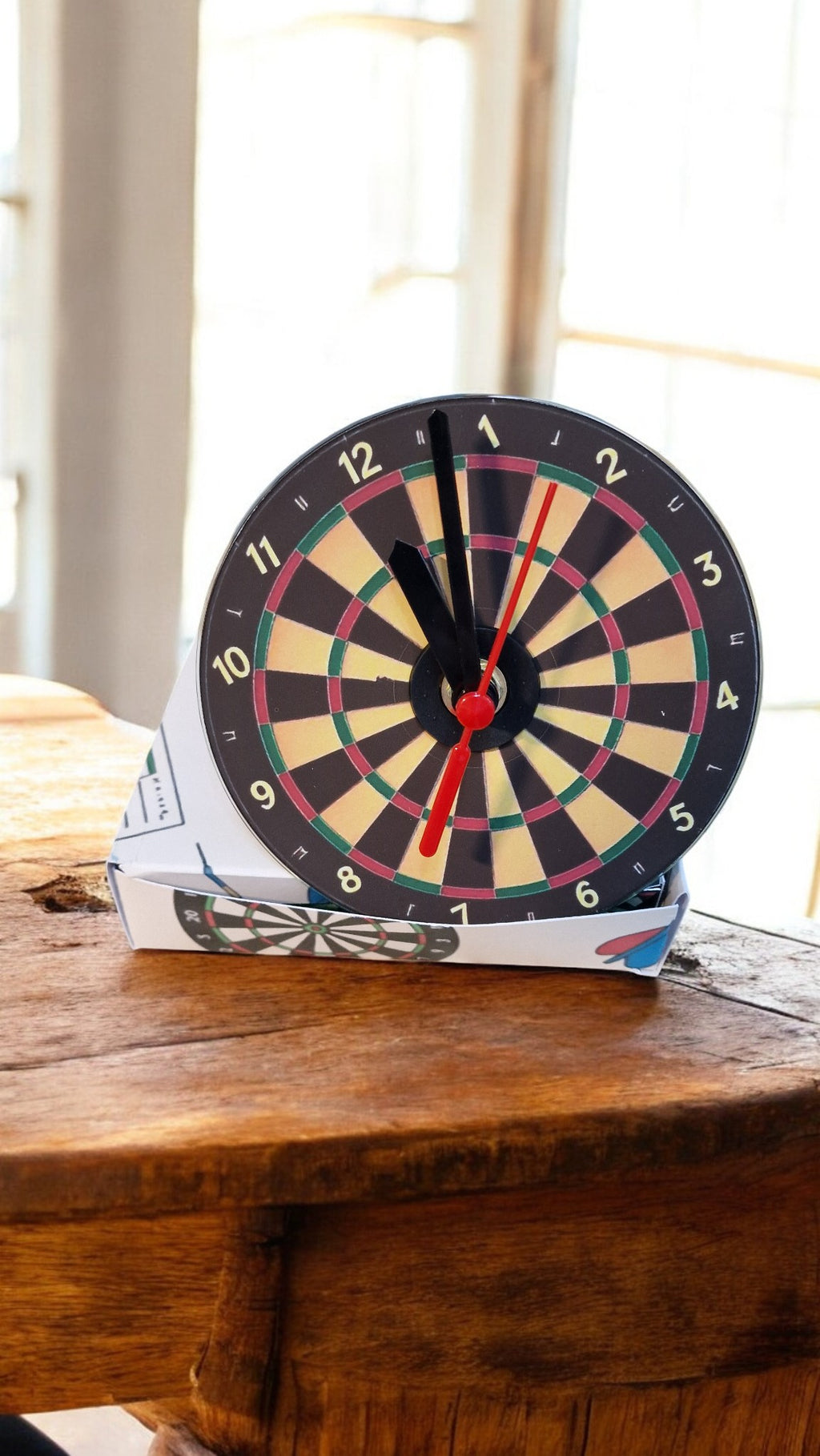 Dartboard clock on a wooden surface with a window in the background