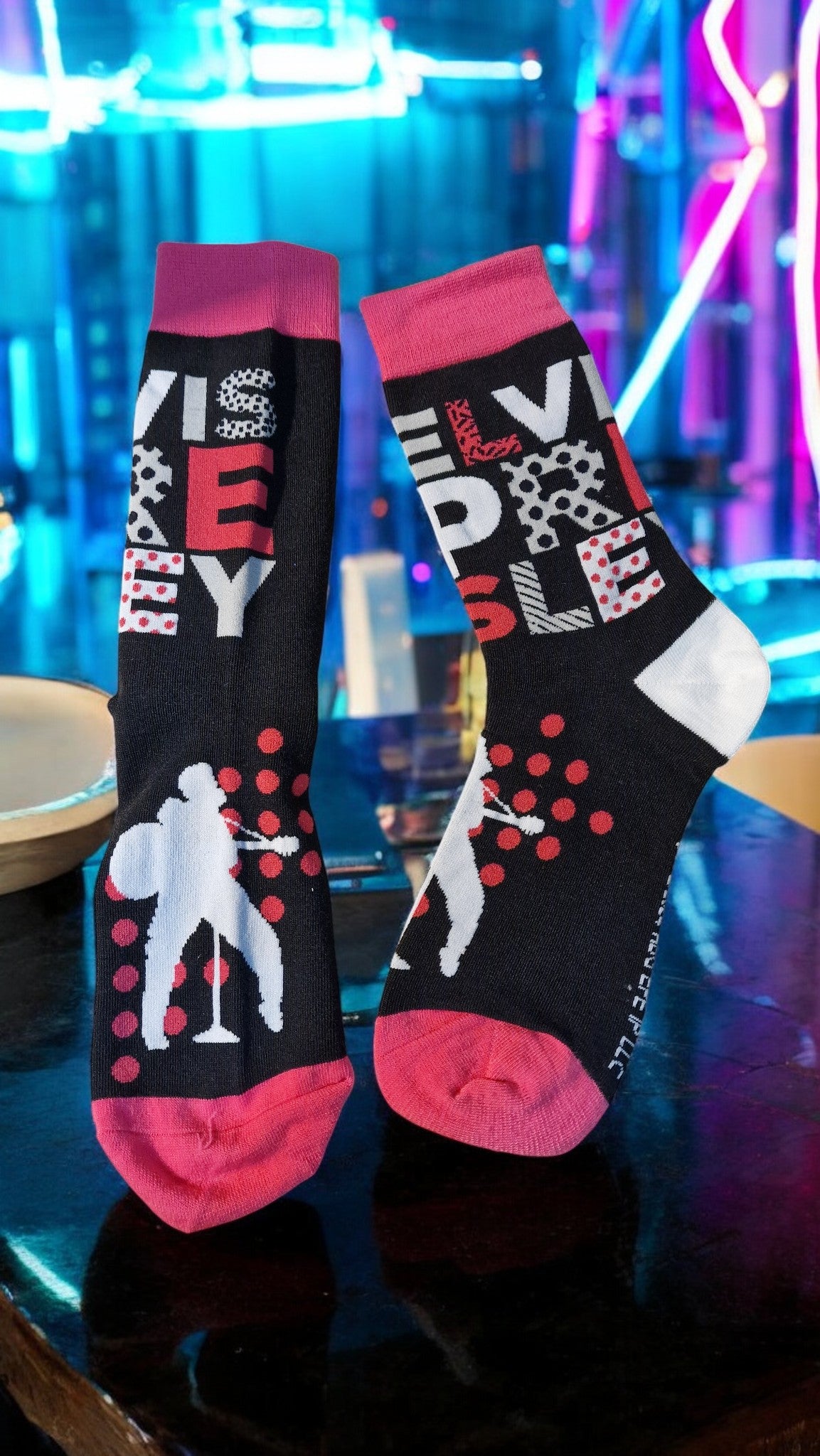 Two socks with colorful designs on a reflective surface with neon lights in the background