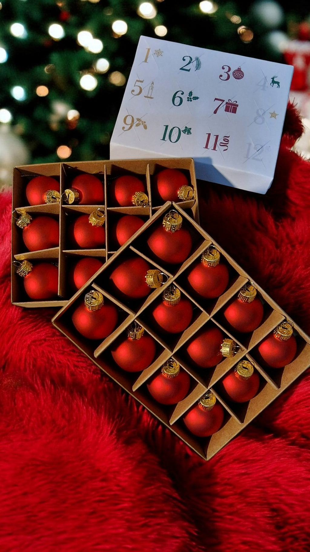 Red Christmas ornaments in a wooden box with a calendar in the background on a red surface.