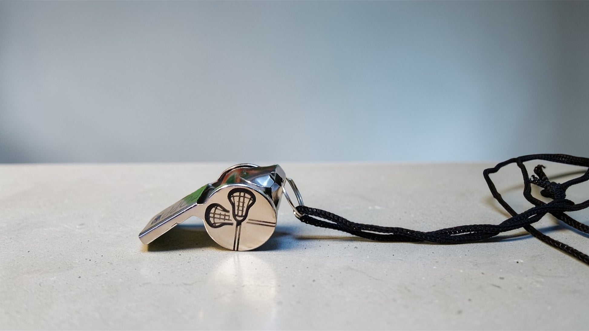 Metallic whistle with a black lanyard on a light surface
