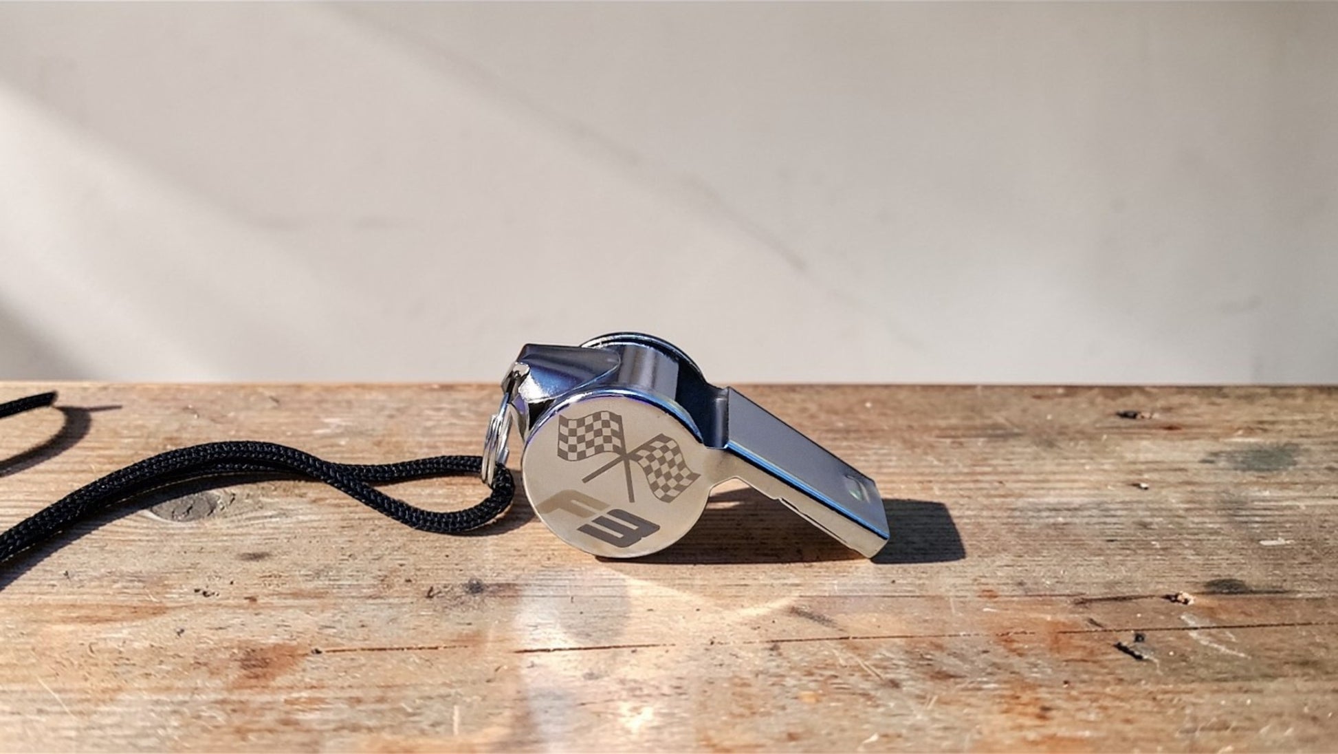 Metallic whistle with a black lanyard on a wooden surface