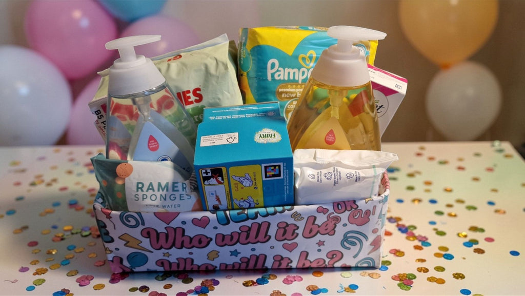 Baby shower gift basket with diapers, bottles, and baby items on a table with balloons in the background.
