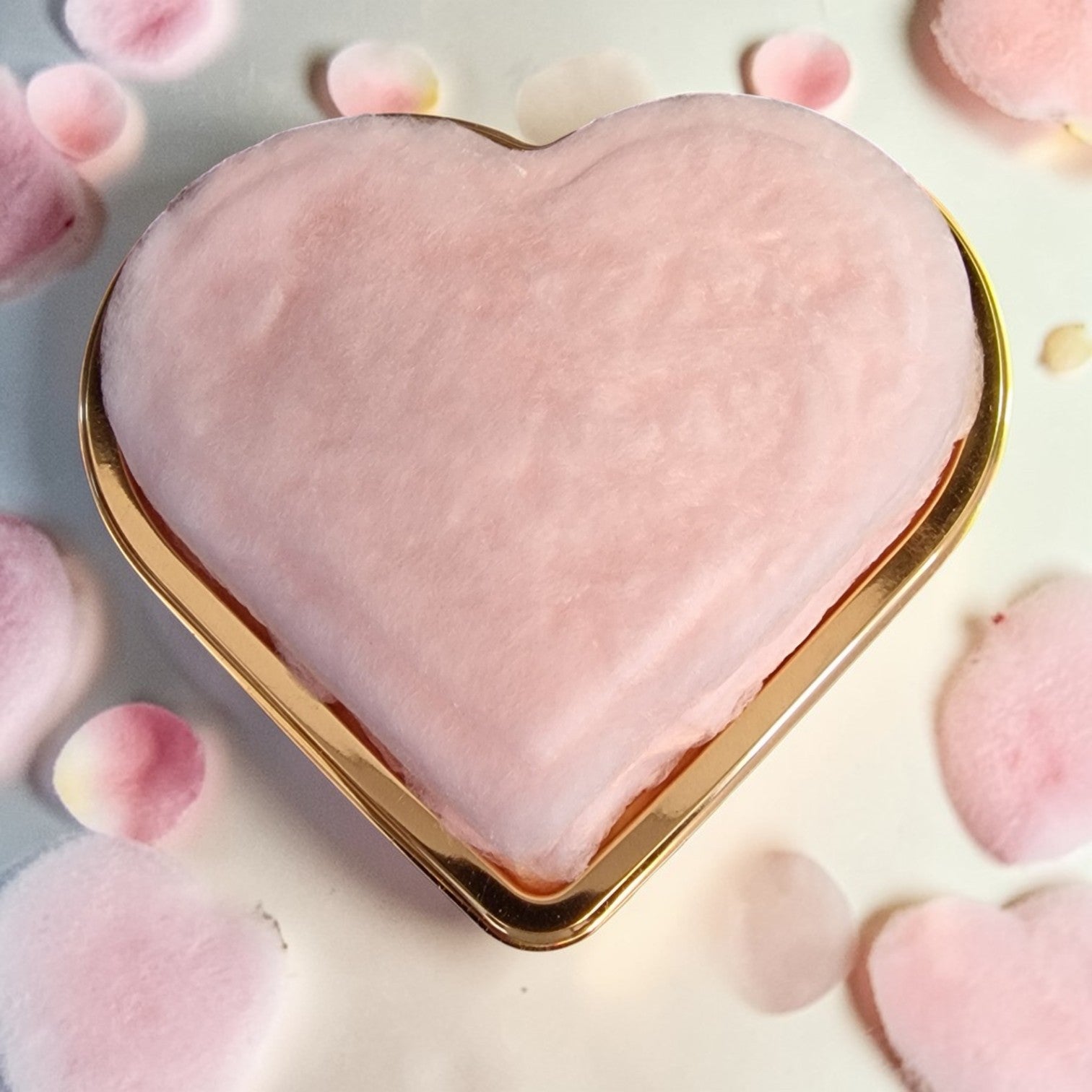 Heart-shaped pink compact with gold border on a soft pink background