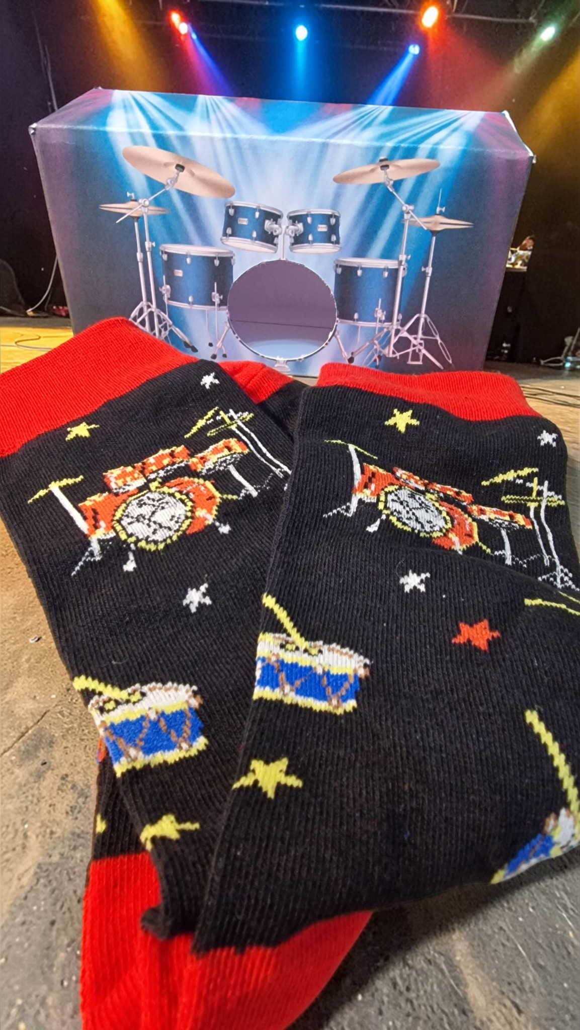 Pair of socks with drum design in front of a drum set backdrop