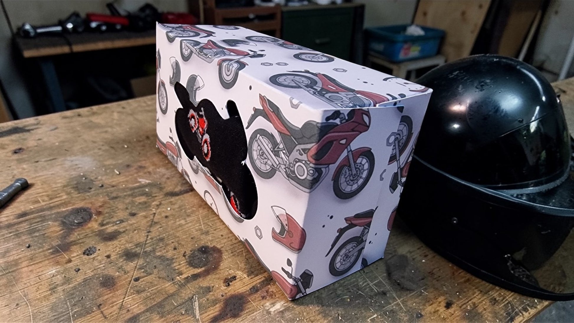 Box with motorcycle design next to a black helmet on a wooden surface