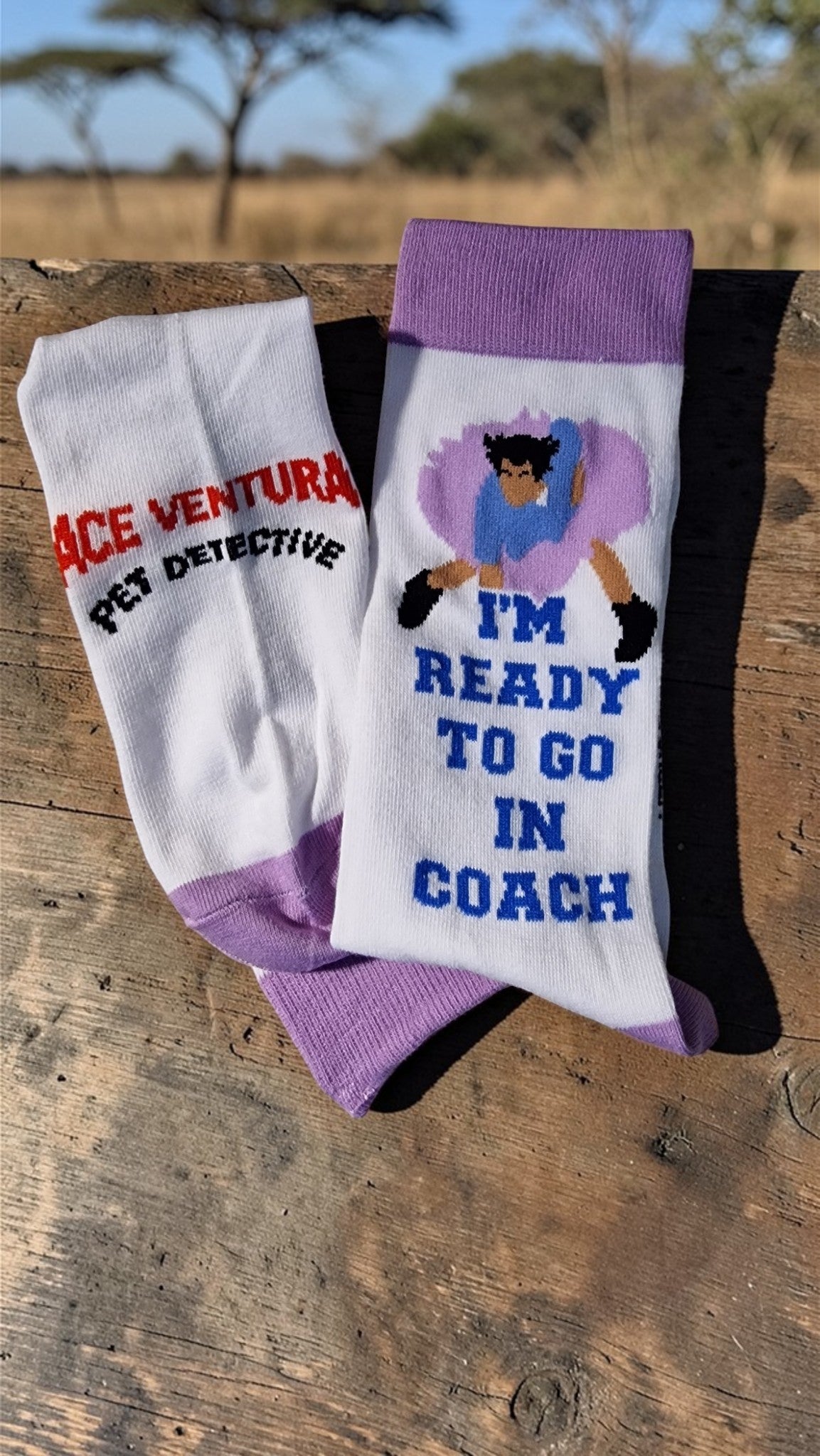 Two pairs of socks with 'Ace Ventura' and 'I'm Ready to Go in Coach' text on a wooden surface.