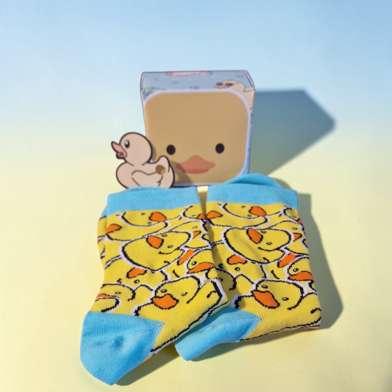 Yellow socks with duck pattern and a small rubber duck toy on a light blue background