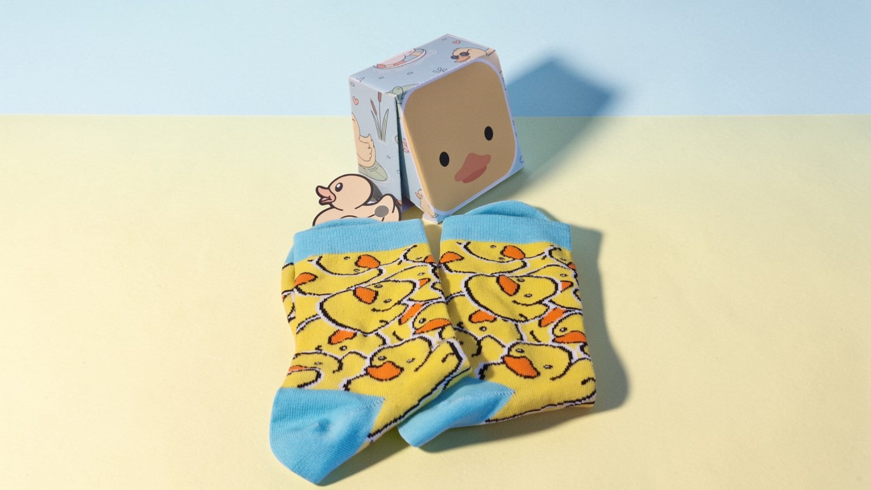 Yellow socks with duck pattern and a matching box on a light blue and beige background