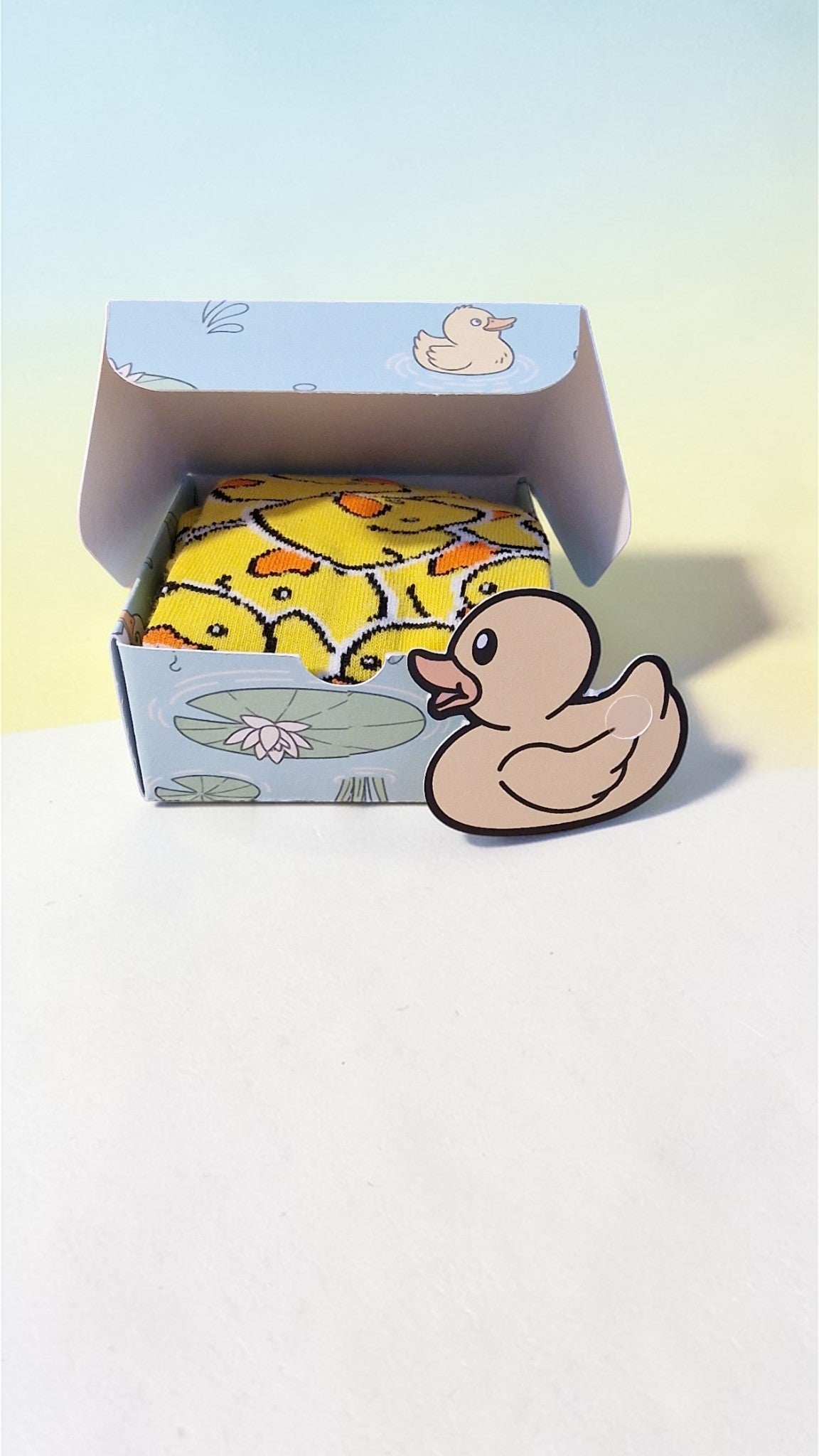 Box of rubber duck toys with a duck-shaped card on a light background
