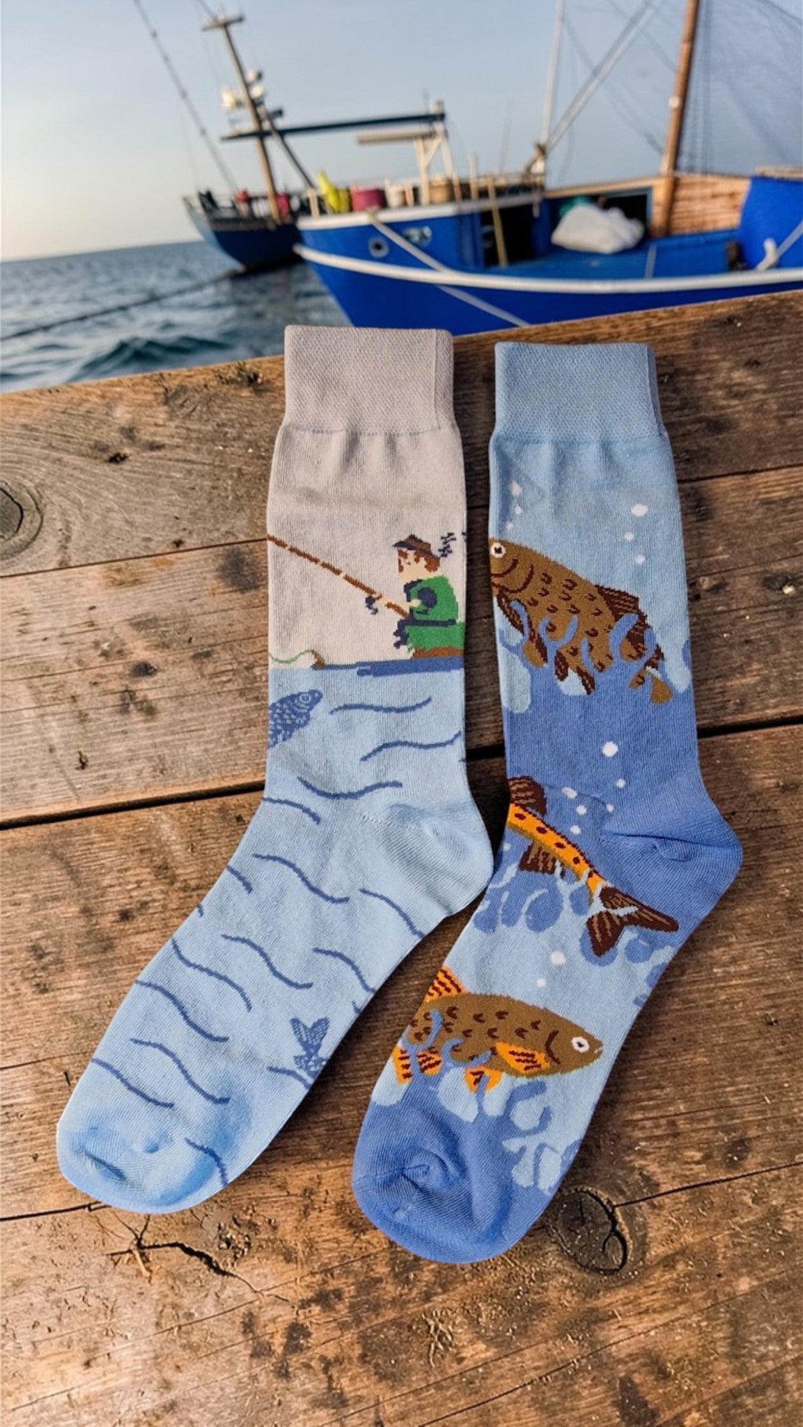 Two socks with fishing design on a wooden surface near water and a boat.