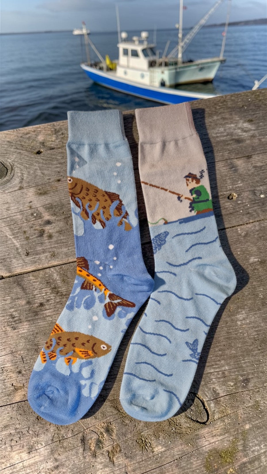 Two pairs of socks with fish and tiger designs on a wooden surface near water.