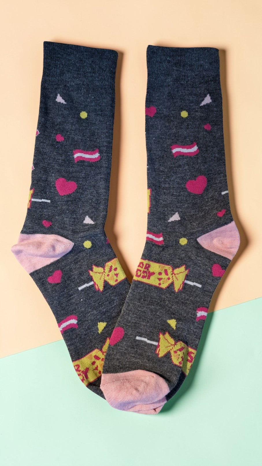 Pair of dark gray socks with colorful candy-themed designs on a light pink background